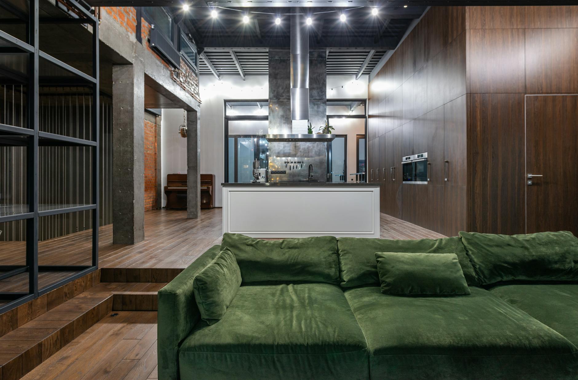 Zielona sofa w salonie połączonym z aneksem kuchennym w loftowym mieszkaniu