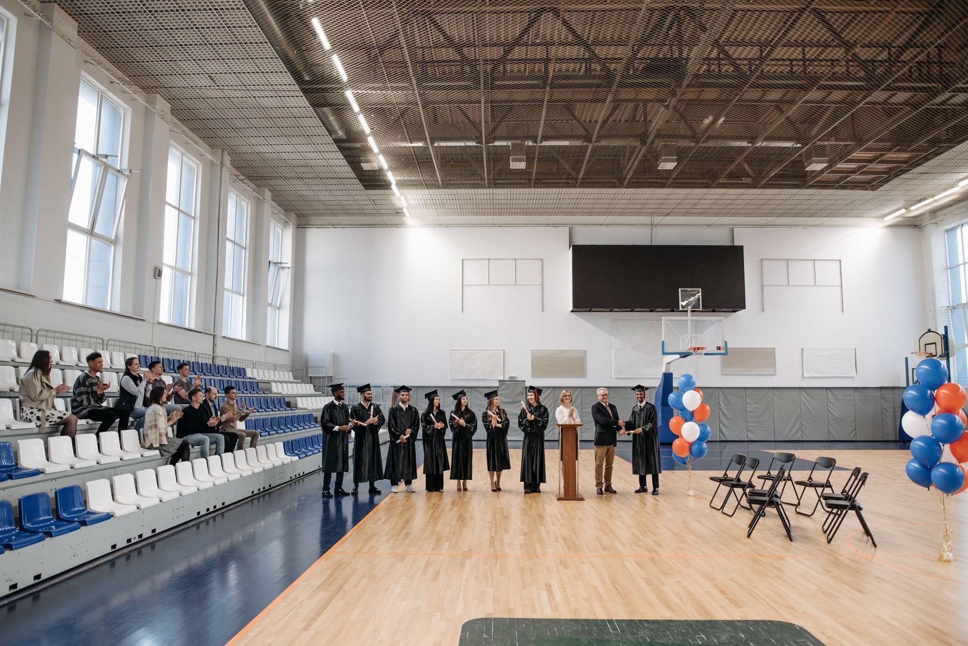 Absolwenci w togach podczas uroczystości rozdania dyplomów na hali sportowej